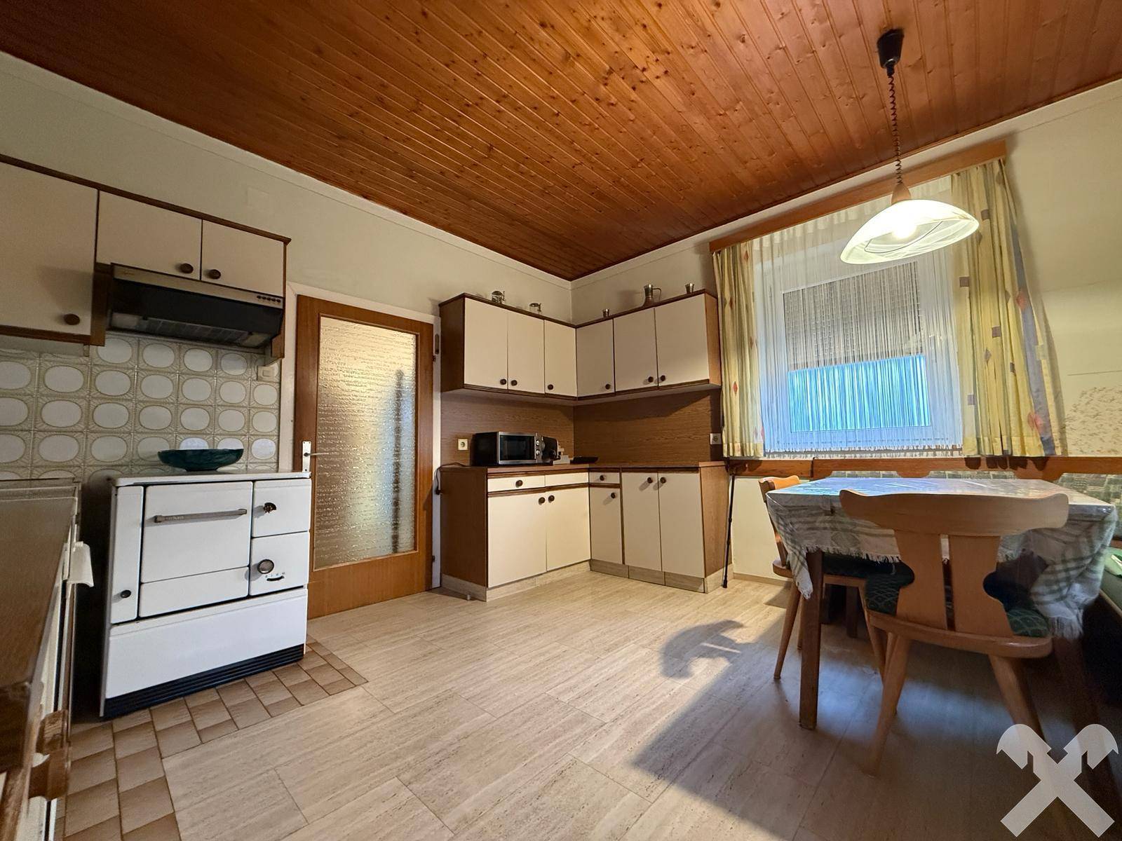 Gemütliche Wohnküche mit Holzbalkendecke, Essbereich und traditionellem Holzherd.