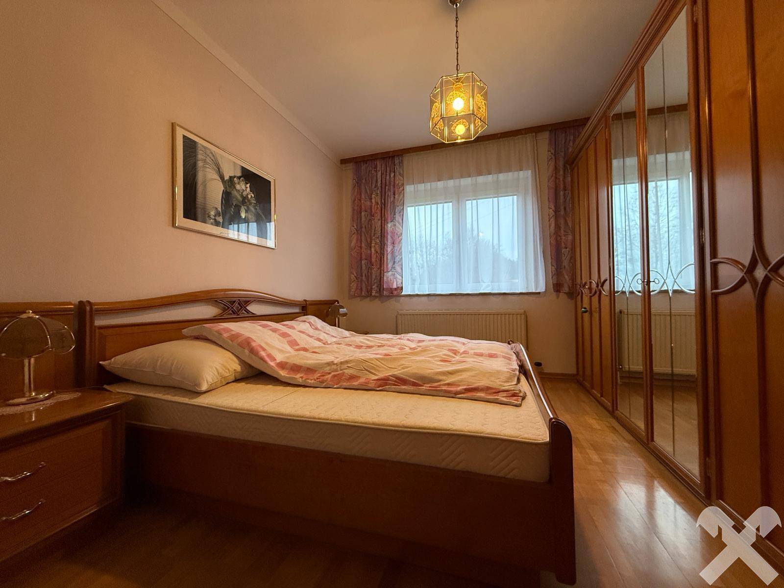 Schlafzimmer mit Holzbett, Parkettboden und großem Spiegelschrank.