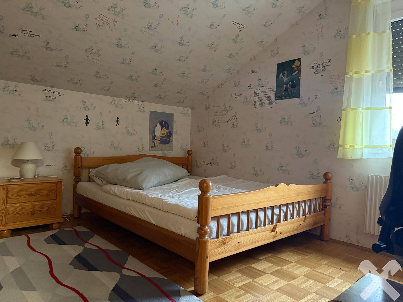 Helles Schlafzimmer im Dachgeschoss mit Holzbett, Parkettboden und Fenster.