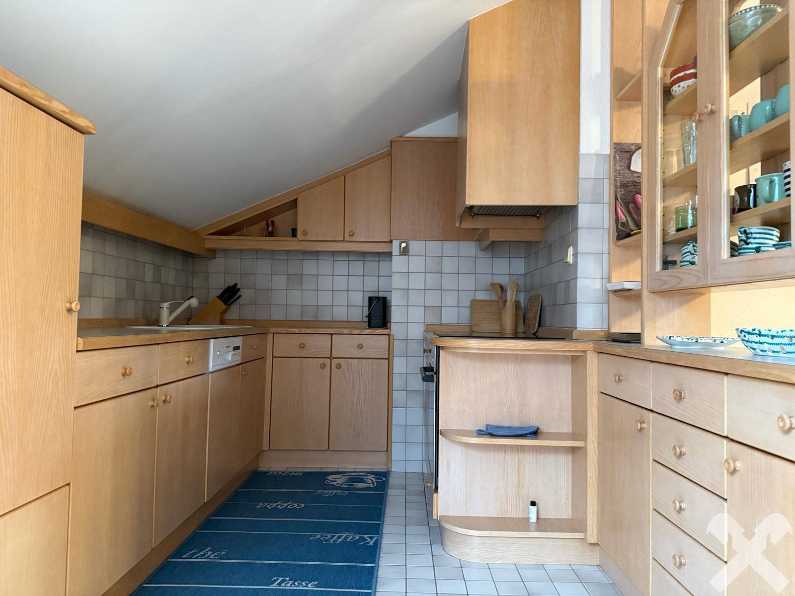 Einbauküche im Dachgeschoss mit Holzschränken, Fliesenboden und Dachschrägen.