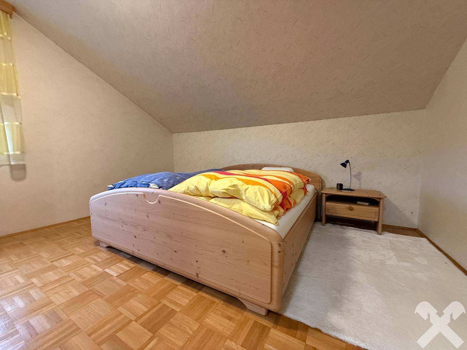 Schlafzimmer im Dachgeschoss mit Holzbett, Parkettboden und Dachschräge.