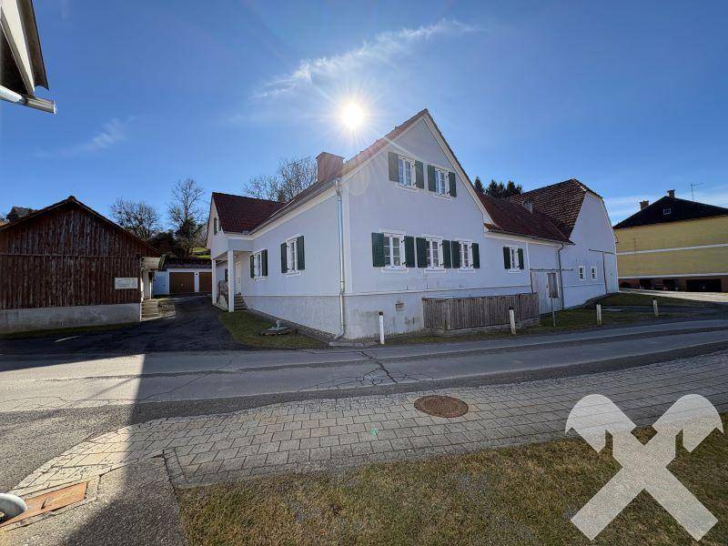 Helles Einfamilienhaus mit Satteldach und grünen Fensterläden in sonniger ländlicher Umgebung.