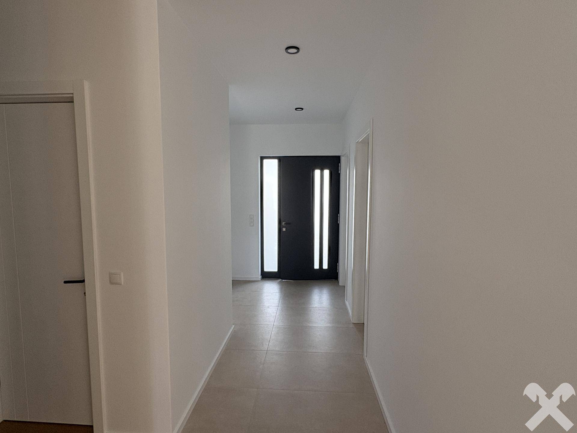 Heller Flur mit modernen Fliesen und einer dunklen Eingangstür, die viel Licht hereinlässt.