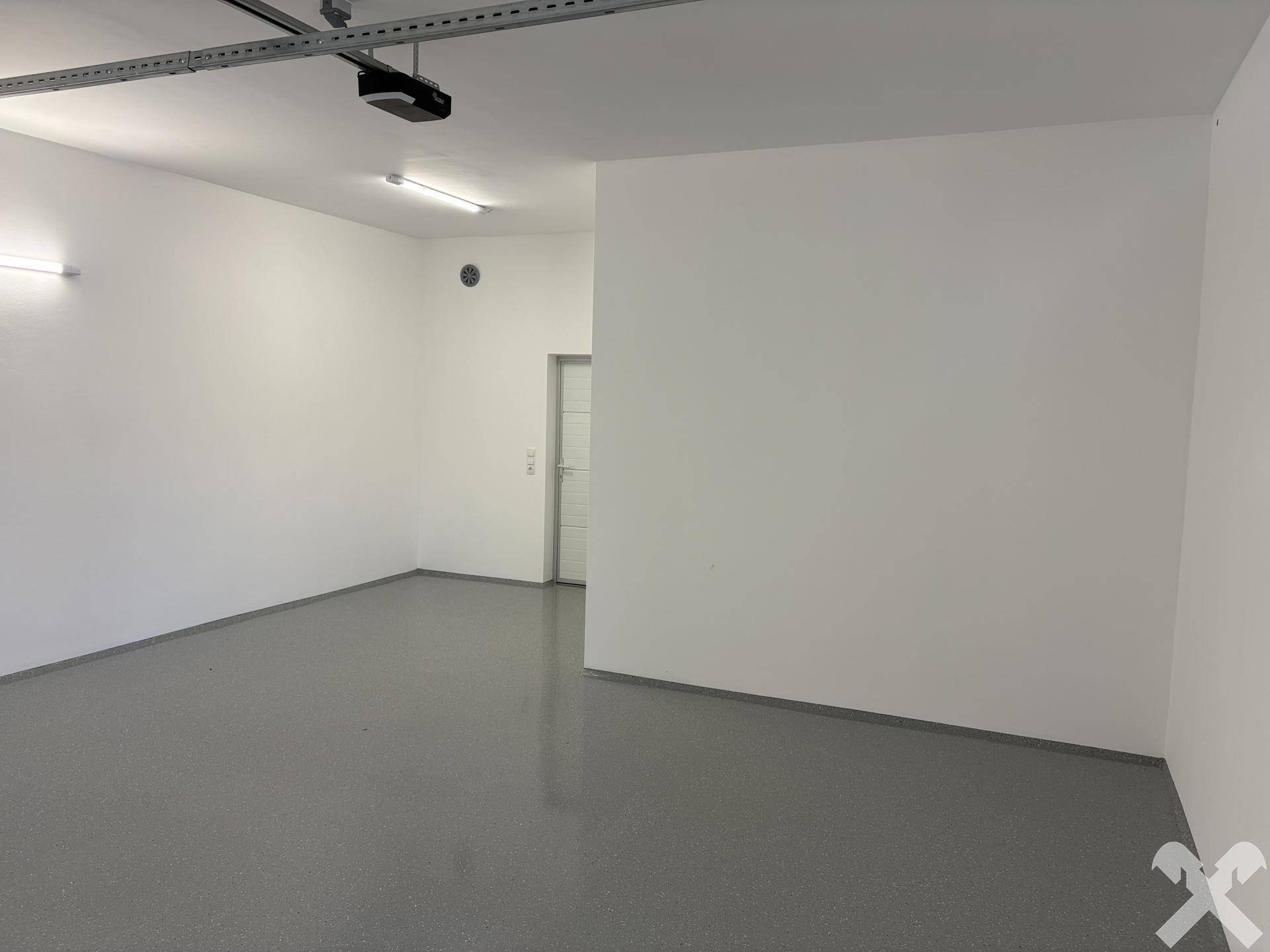 Leere, saubere Garage mit weiß gestrichenen Wänden und glattem, grauem Boden.