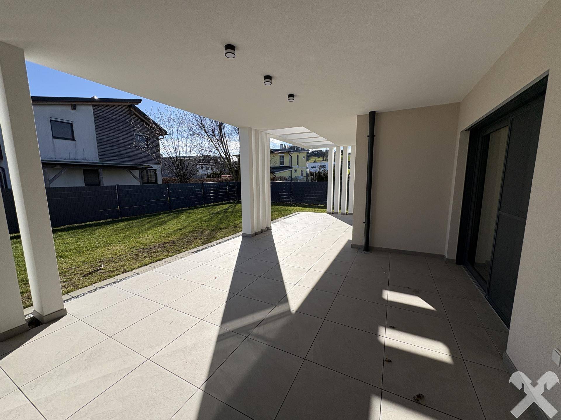 Überdachte Terrasse mit modernen Fliesen, integrierten Lichtern und Blick auf den Garten.