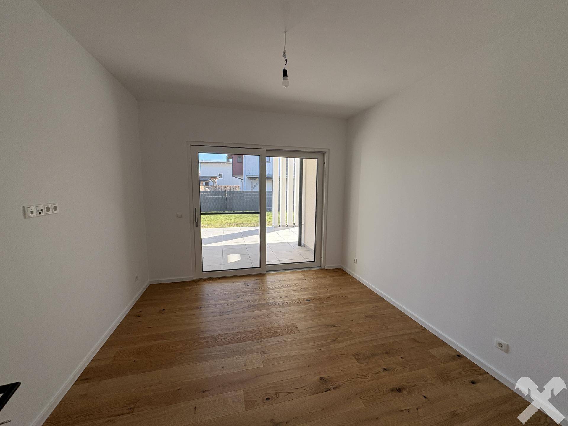 Helles Zimmer mit Holzboden und großen Schiebetüren, die Zugang zum Gartenbereich bieten.