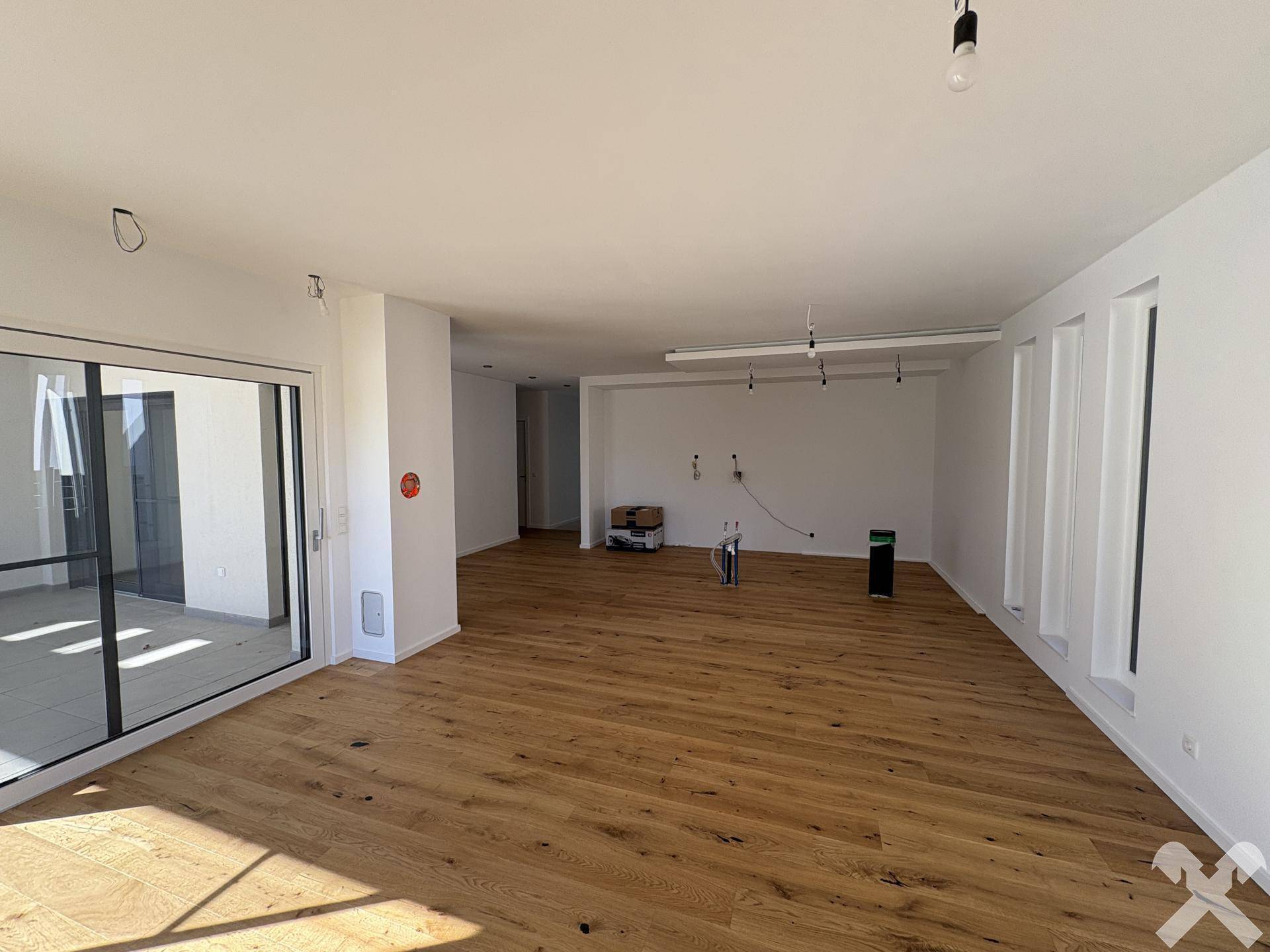 Großzügiger, leerer Wohnbereich mit Holzboden und Zugang zur Terrasse durch große Schiebetüren.