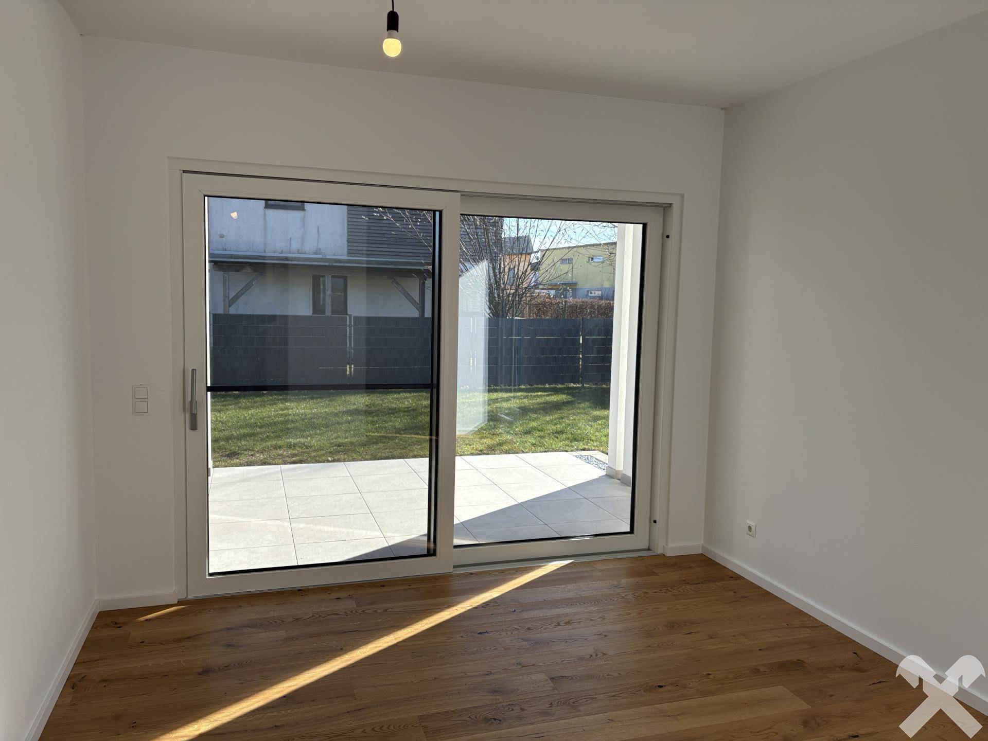 Lichtdurchflutetes Zimmer mit Holzboden und breiter Schiebetür, die auf die Terrasse führt.