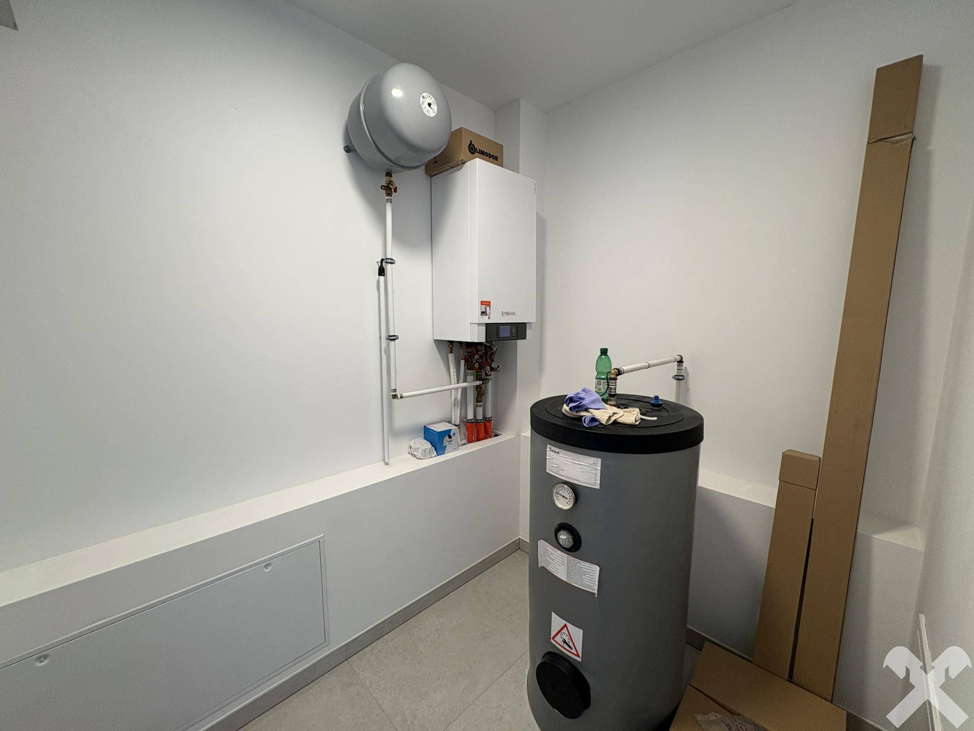 Technikraum mit Warmwasserspeicher und Heizungsanlage, ordentlich an der Wand montiert.