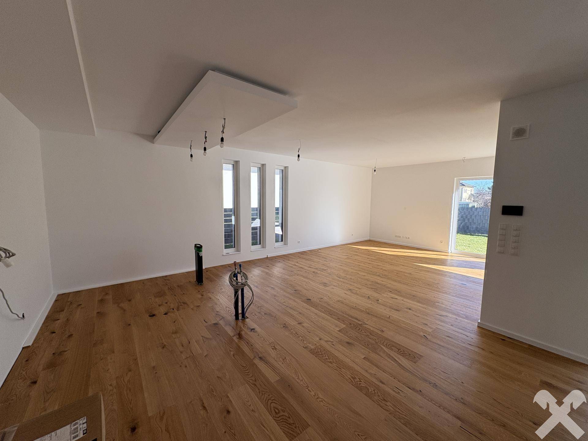 Großer, heller Wohnbereich mit Holzboden und mehreren hohen Fenstern, die viel Licht spenden.