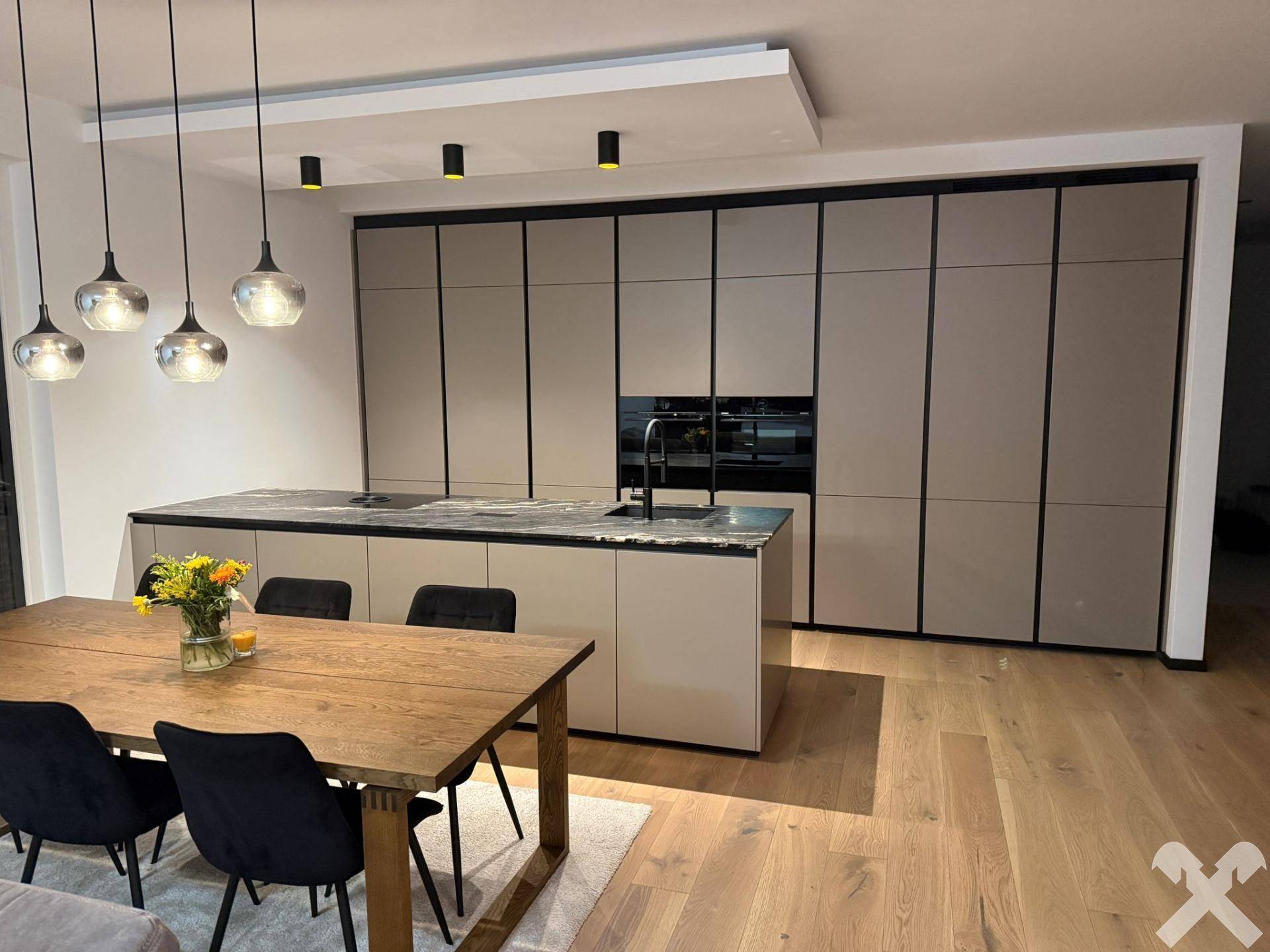Moderne Einbauküche mit Kücheninsel, dunkler Arbeitsplatte und Essbereich mit Holztisch.