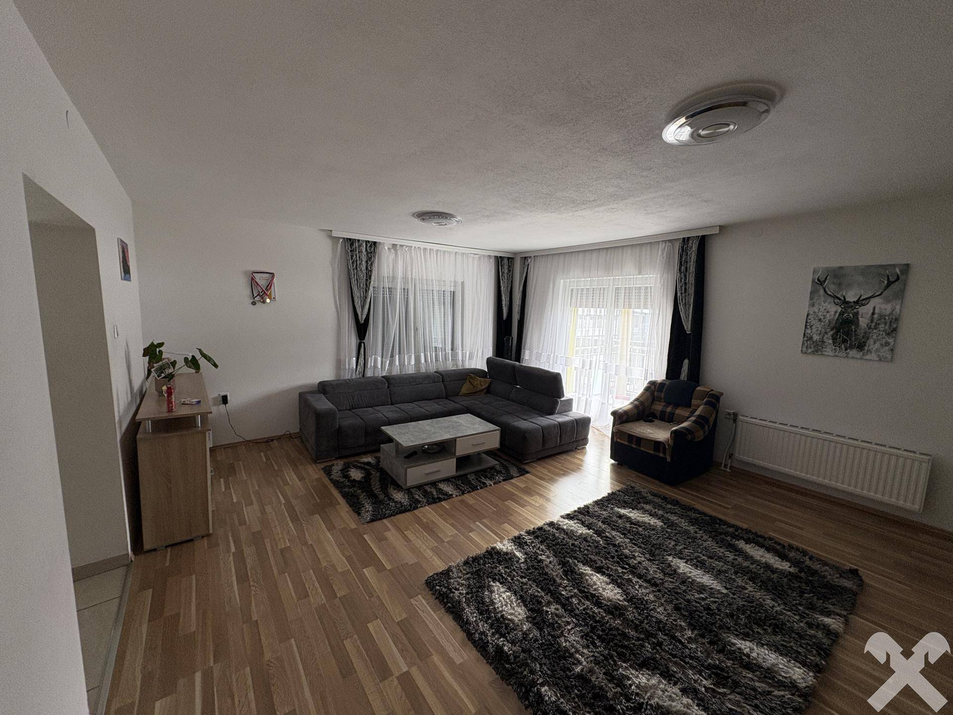 Gemütliches Wohnzimmer mit Parkettboden, großem Sofa und Zugang zum Balkon.