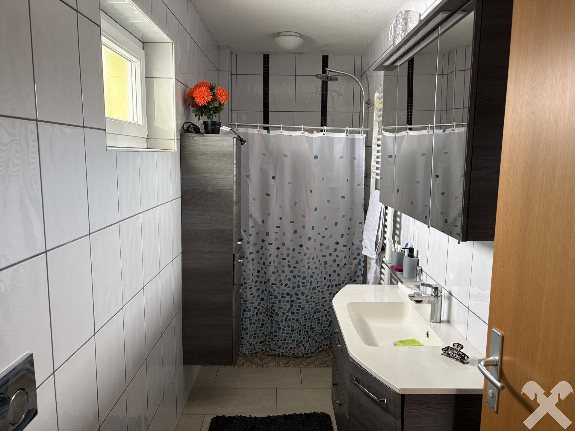 Modern gefliestes Badezimmer mit Dusche, Waschbecken und Spiegelschrank.