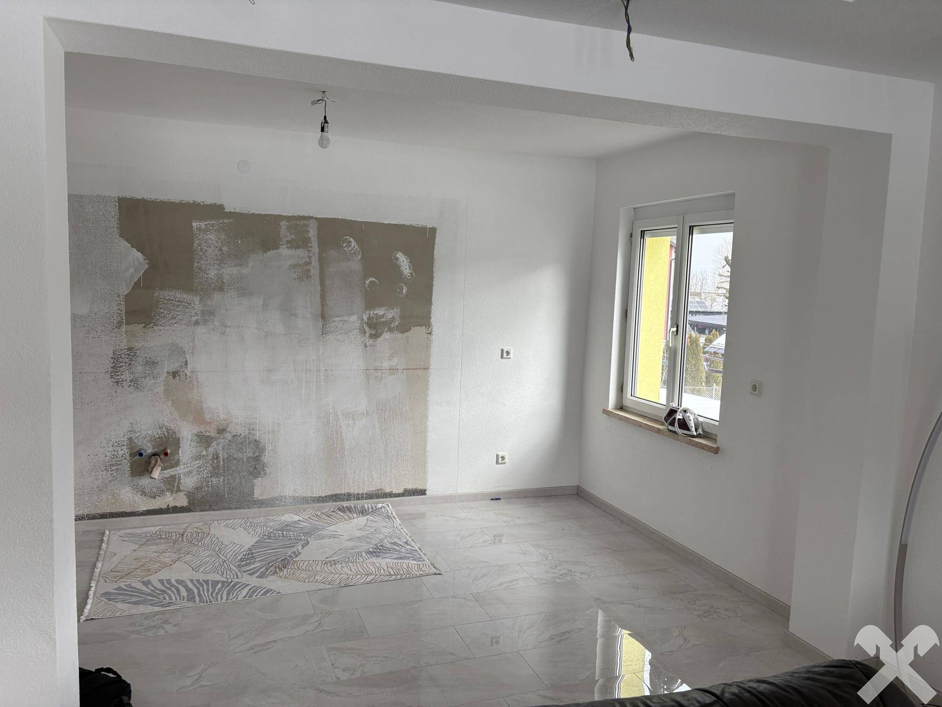 Unfertiger Wohnbereich mit Fliesenboden und vorbereiteter Wand für weitere Gestaltung.