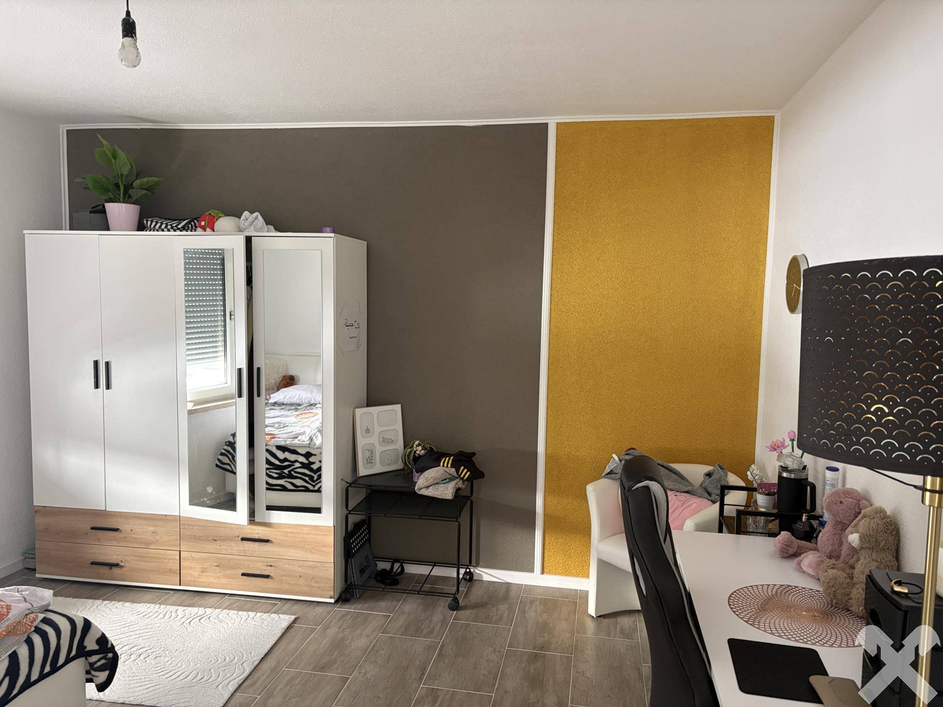 Schlafzimmer mit Kleiderschrank, Schreibtisch und farbiger Wandgestaltung.