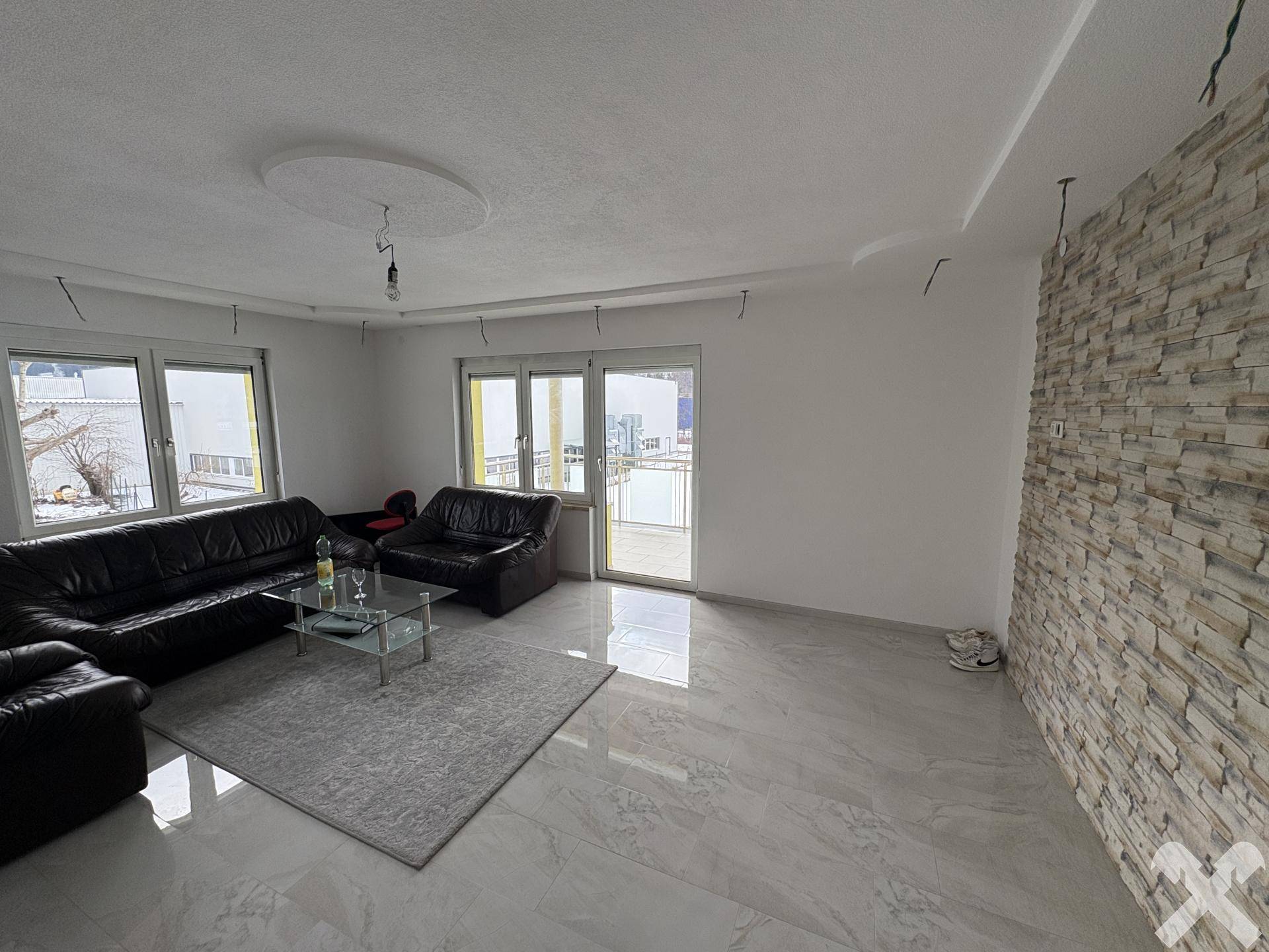 Wohnzimmer mit Ledersofas, Fliesenboden und dekorativer Steinwand.