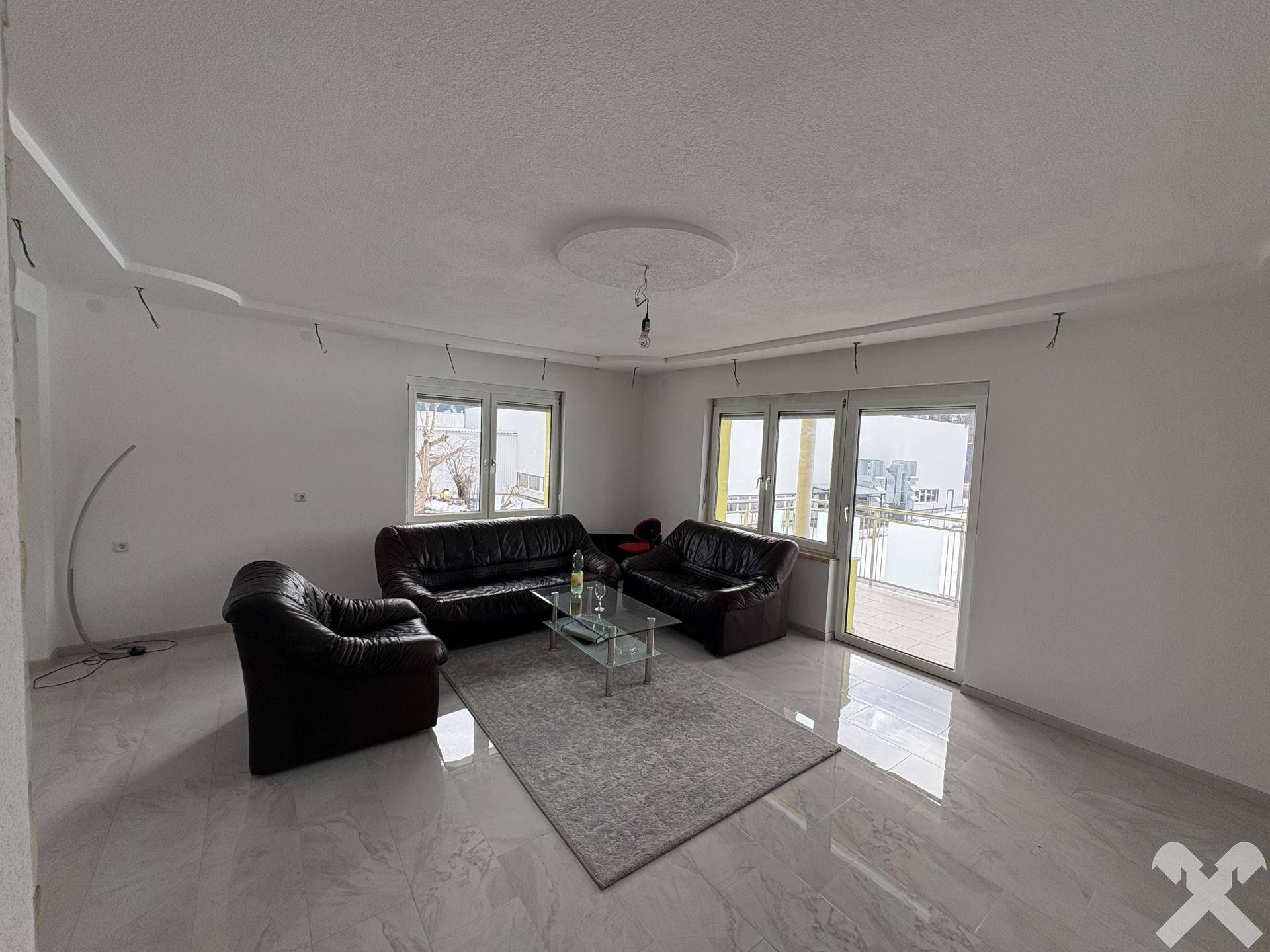 Geräumiges Wohnzimmer mit Ledersofas, Couchtisch und Zugang zum Balkon.