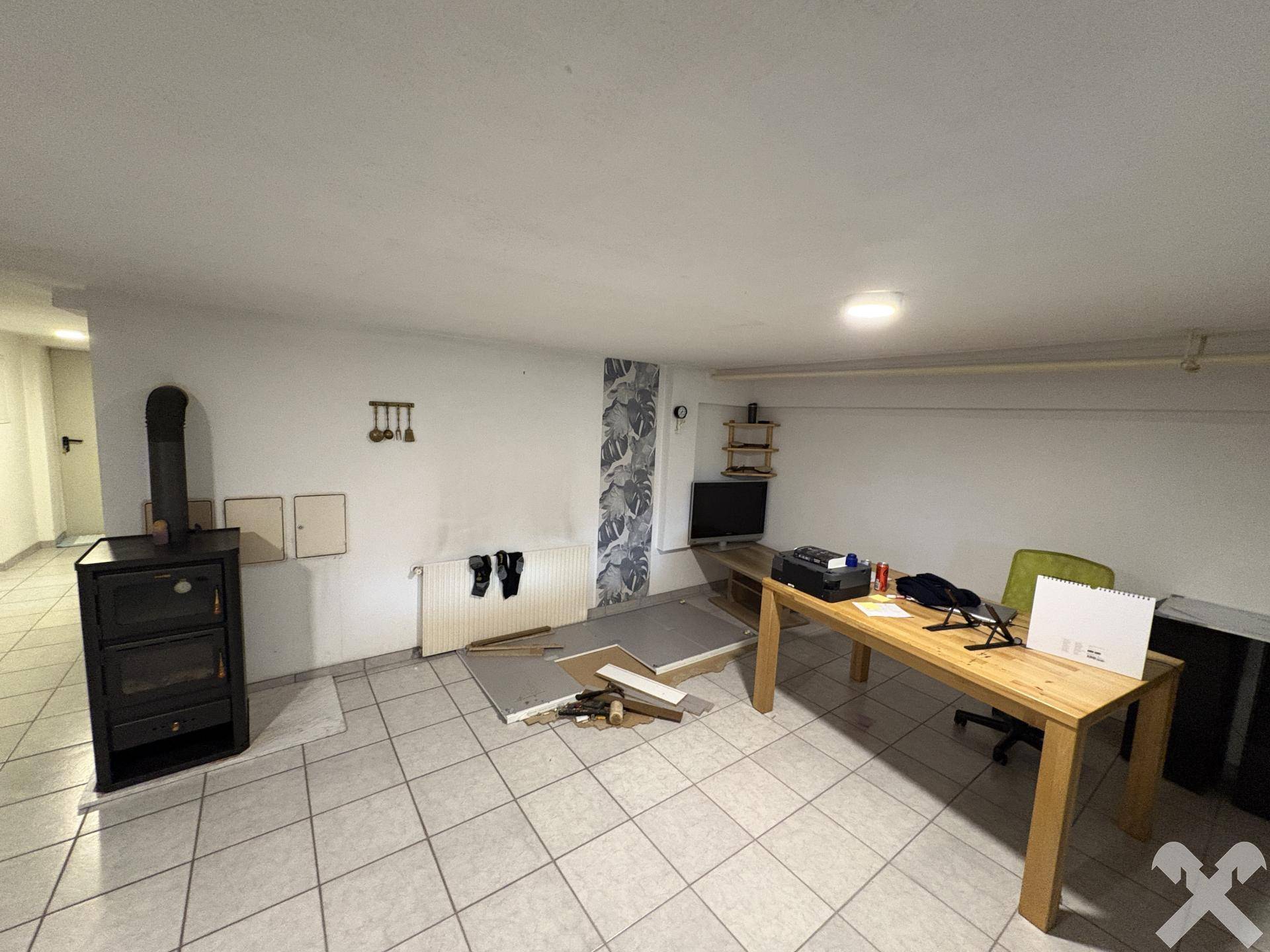 Kellerraum mit Holzofen, Arbeitsbereich und Fliesenboden.