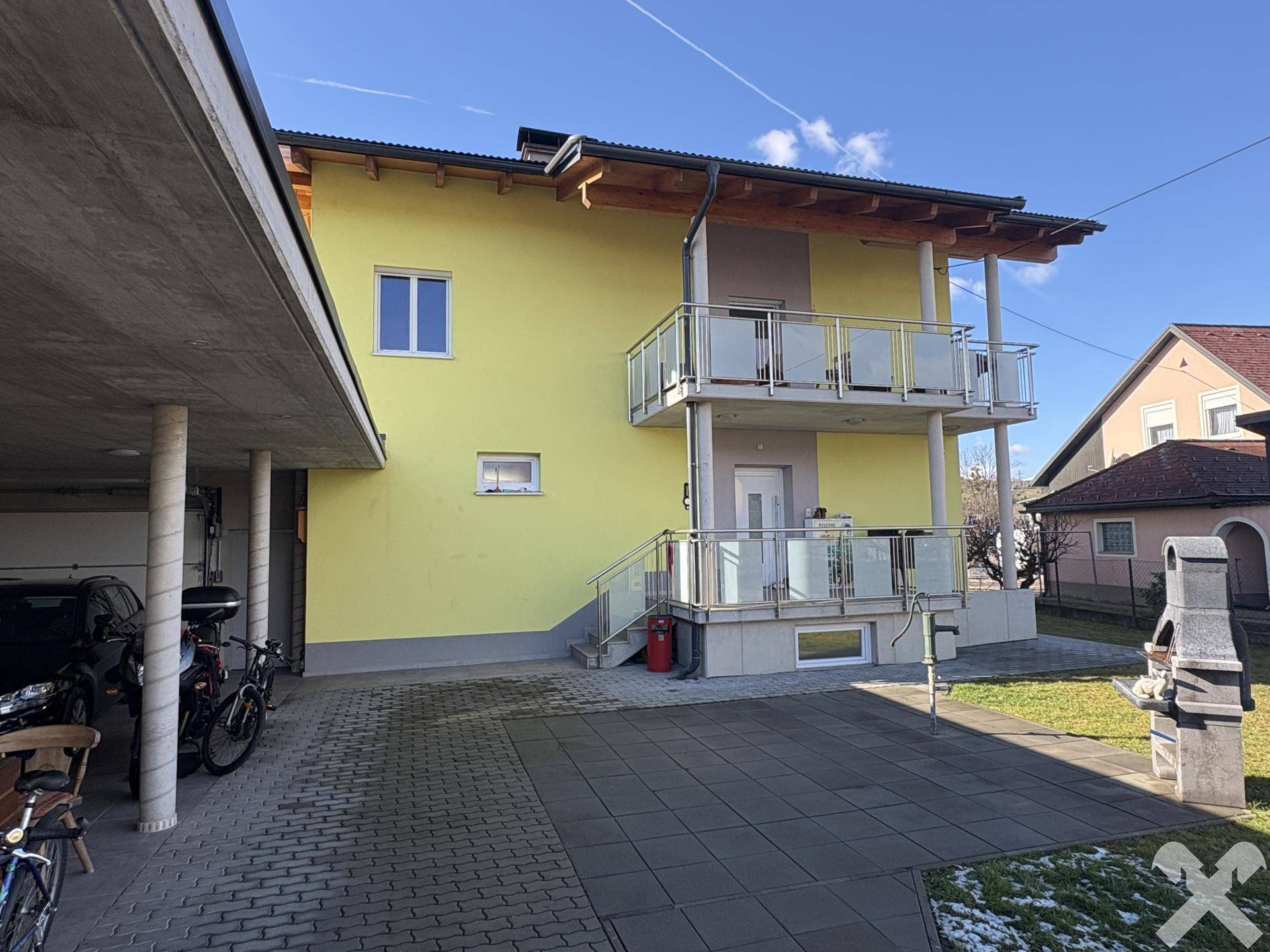 Rückseite des Hauses mit zwei Balkonen, Außentreppe und gepflastertem Bereich mit Grill.