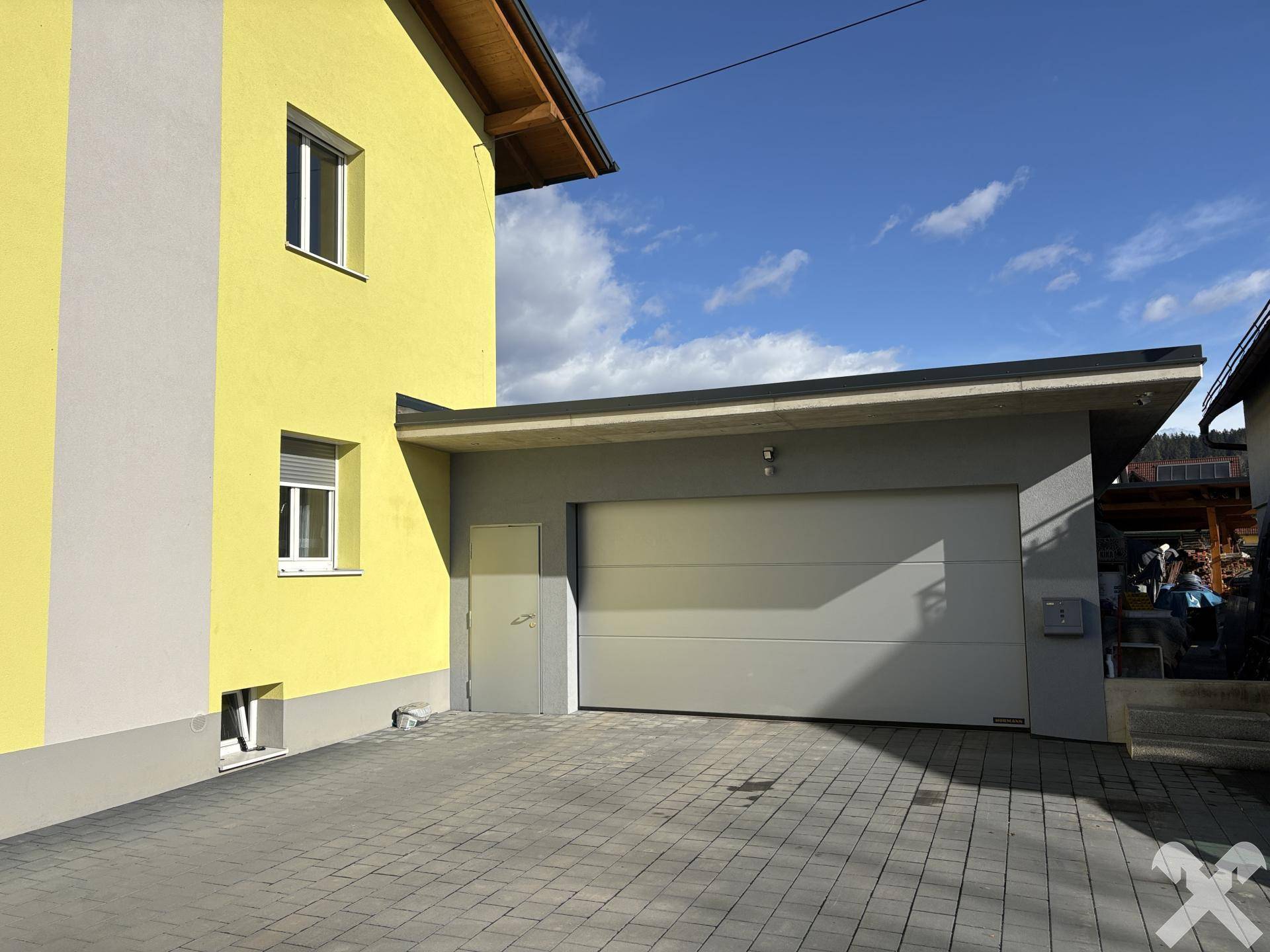 Moderne Garage mit Sektionaltor und direktem Zugang zum gelb gestrichenen Haus.