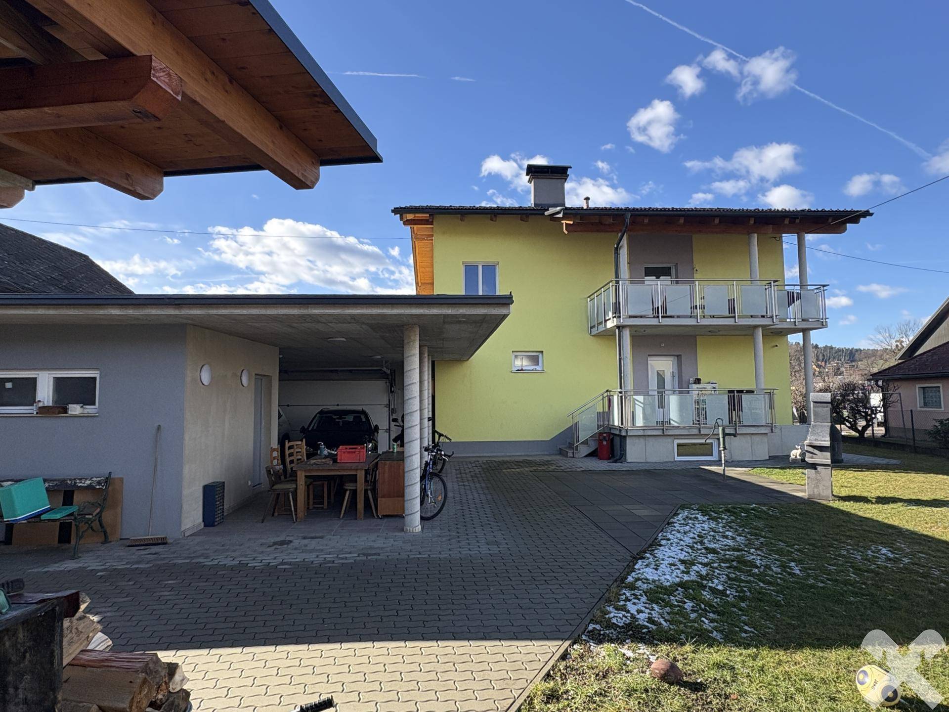 Gesamtansicht des Hauses mit Carport, Garten und Balkonen unter einem weiten Himmel.