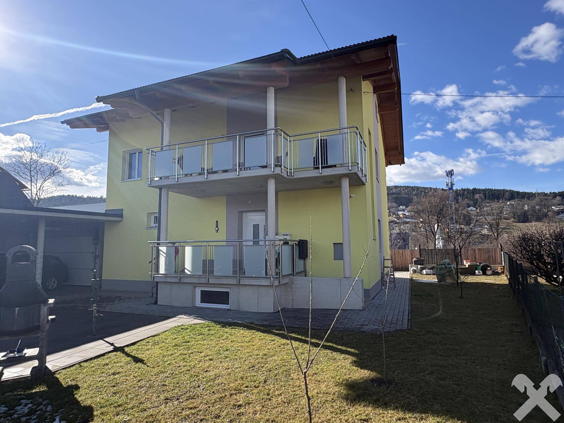 Vorderansicht des Hauses mit Balkonen und einem gepflegten Rasenbereich im Sonnenschein.