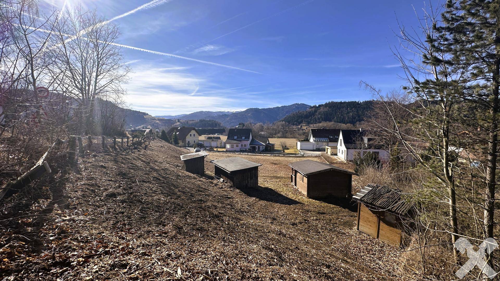 Blick über ein leicht abfallendes Grundstück mit kleinen Schuppen und Häusern im Tal.