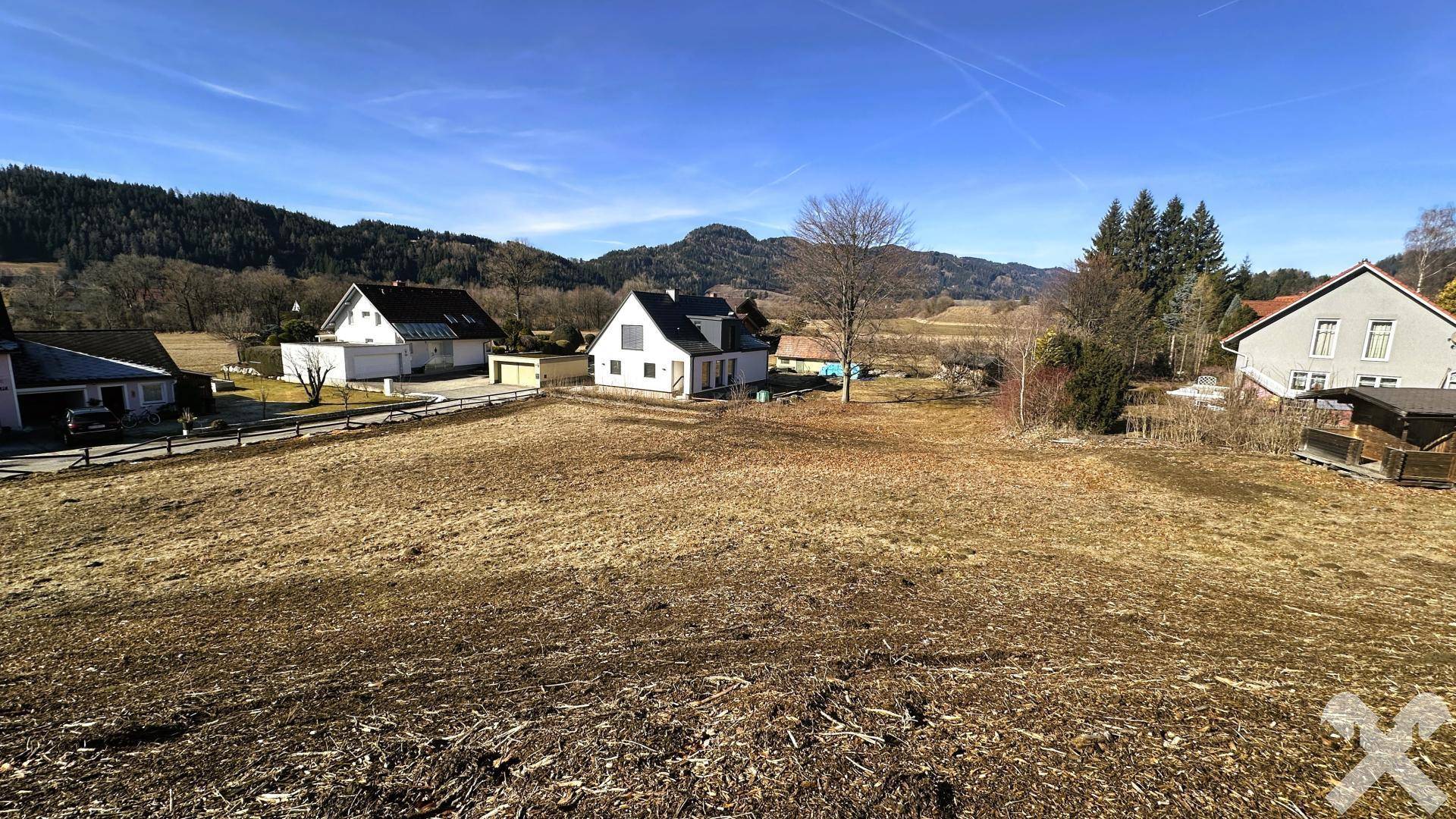 Großes, offenes Grundstück mit Blick auf die umliegende Bebauung und die bewaldeten Berge.