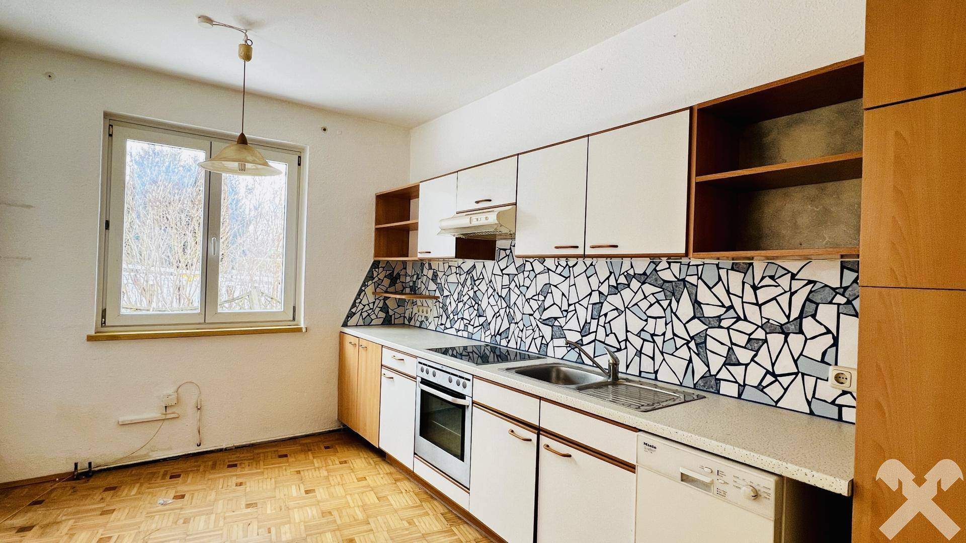 Küche mit älterer Einbauküche, Fliesenboden und Fenster mit Blick ins Grüne.