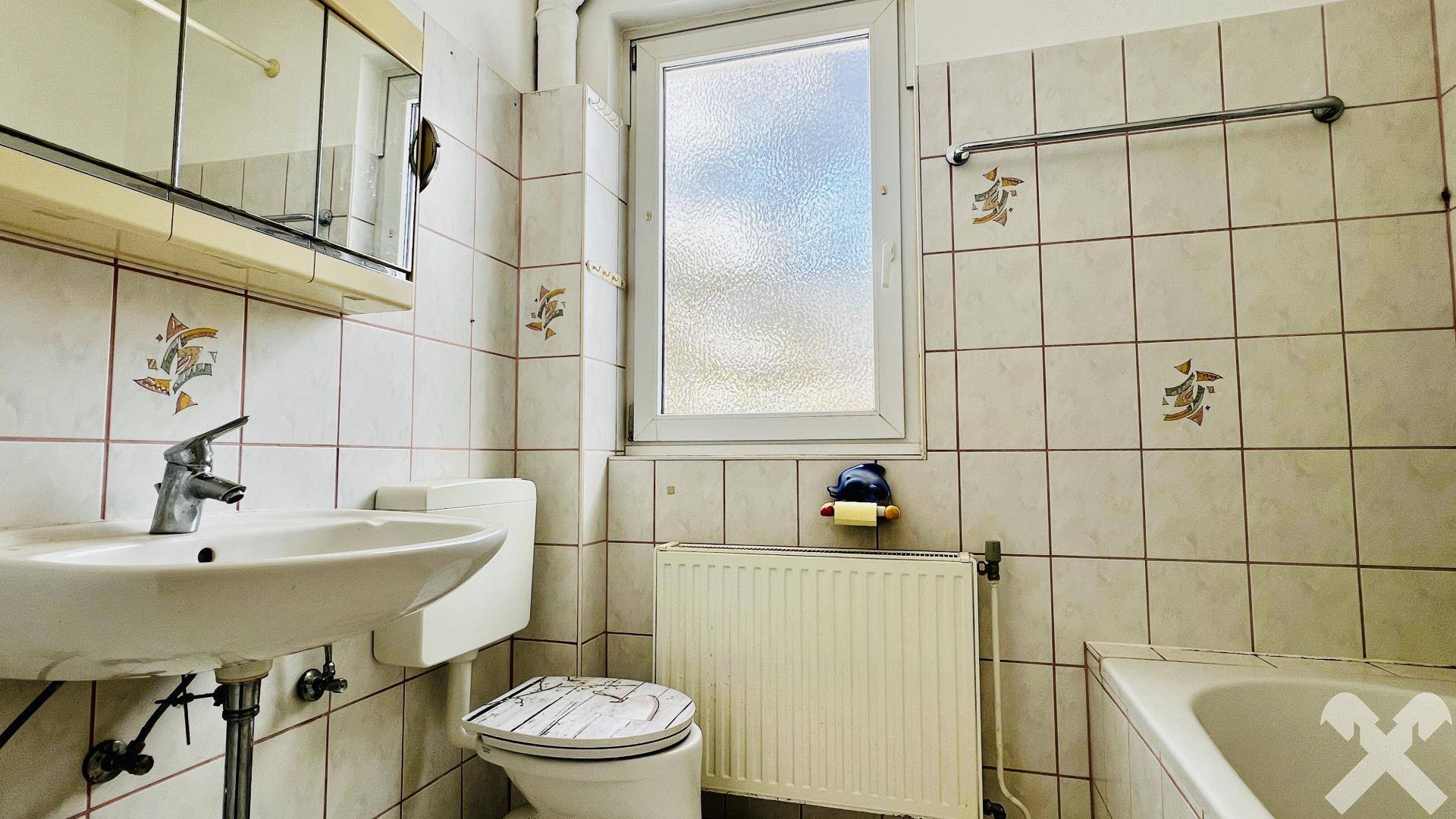 Gefliestes Badezimmer mit Badewanne, Waschbecken, WC und Fenster für Tageslicht.