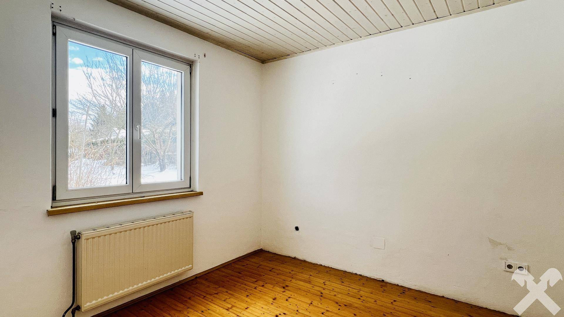 Helles Zimmer mit Holzboden, Fenster und Heizkörper, ideal als Schlaf- oder Arbeitszimmer.