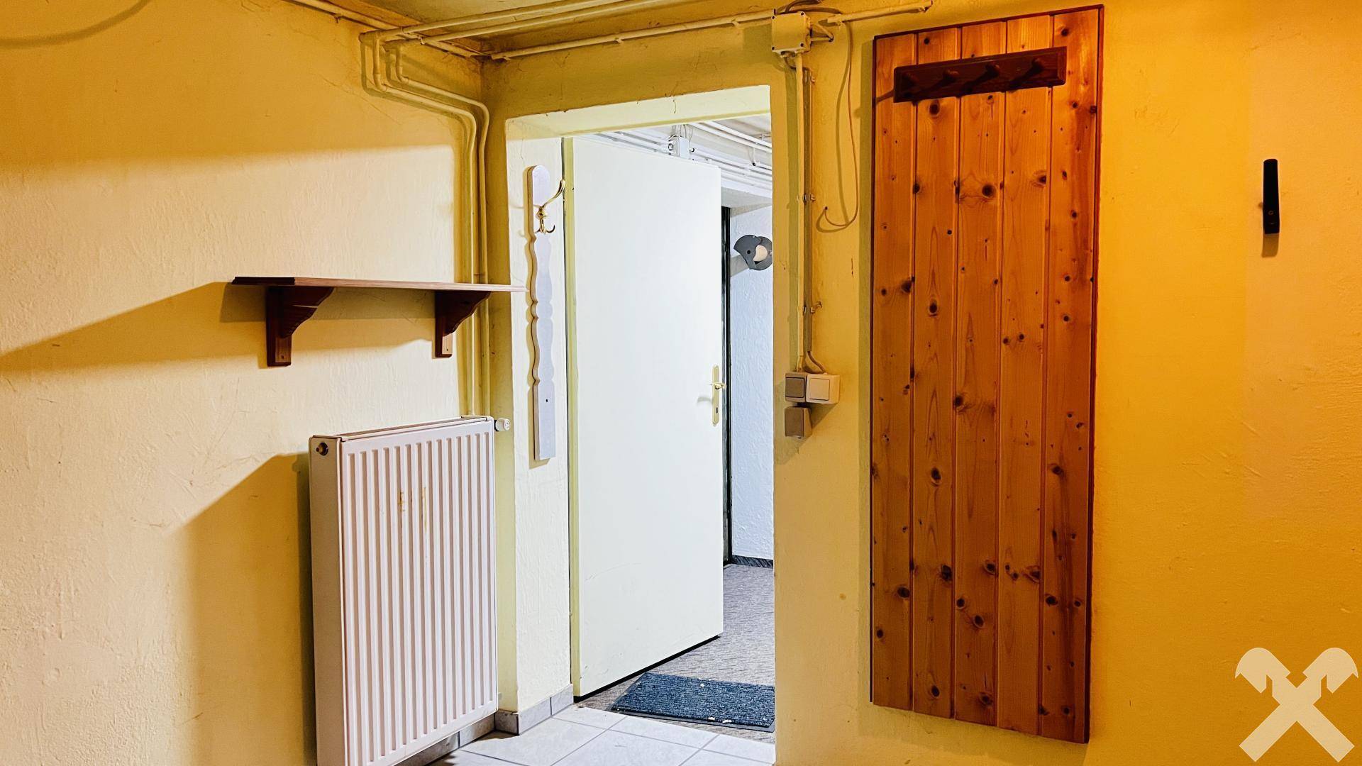 Flur mit Heizkörper, Holztür und einfacher Einrichtung, führt zu weiteren Räumen.