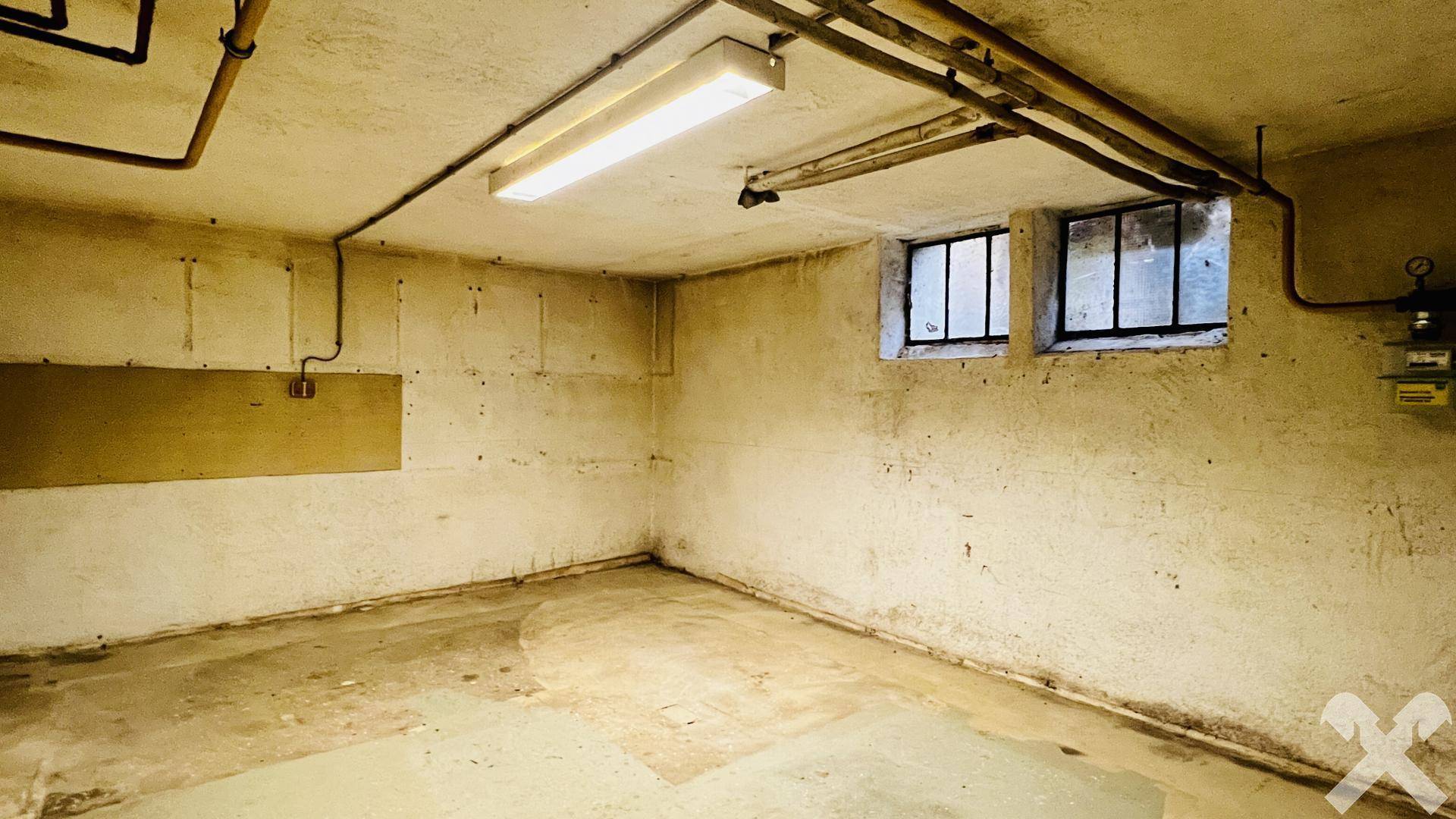 Unausgebauter Kellerraum mit kleinen Fenstern und sichtbaren Leitungen, bietet Stauraum.
