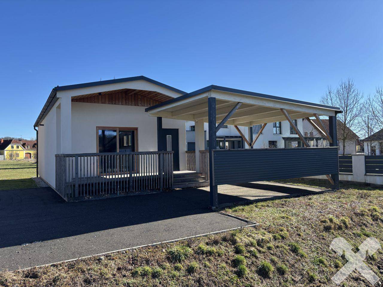 Modernes Einfamilienhaus mit heller Fassade, Holzdetails und einem praktischen Carport unter blauem Himmel.