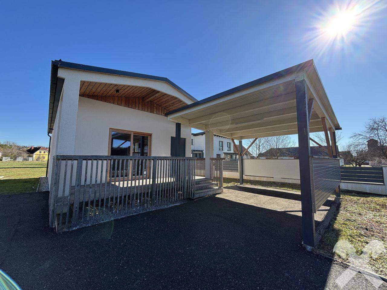Sonnige Ansicht des modernen Hauses mit Holzverkleidung und überdachtem Stellplatz für Fahrzeuge.