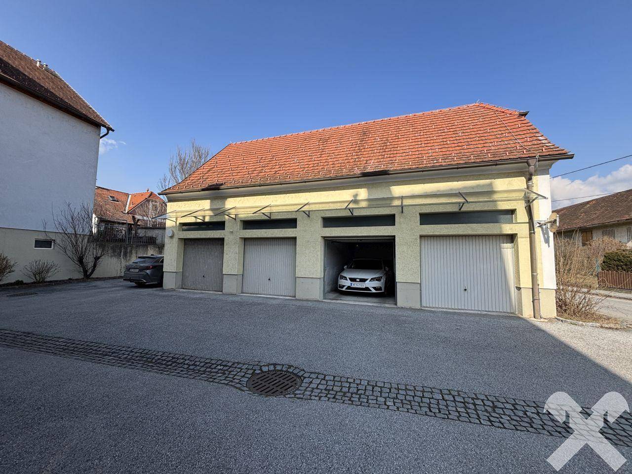 Separate Garagenreihe mit mehreren Stellplätzen und rotem Ziegeldach unter blauem Himmel.