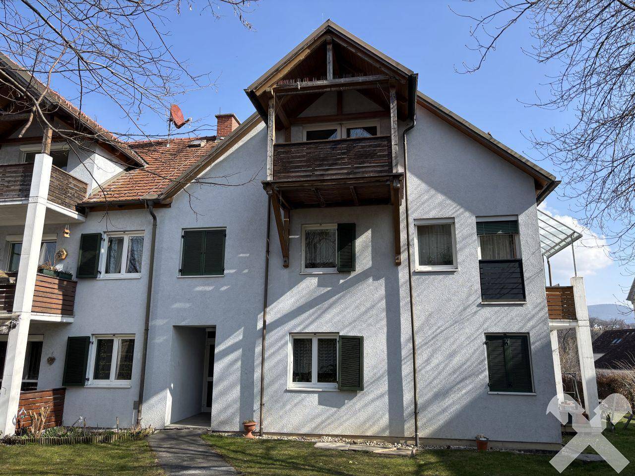 Wohngebäude mit mehreren Balkonen, grüner Rasenfläche und traditionellem Ziegeldach.