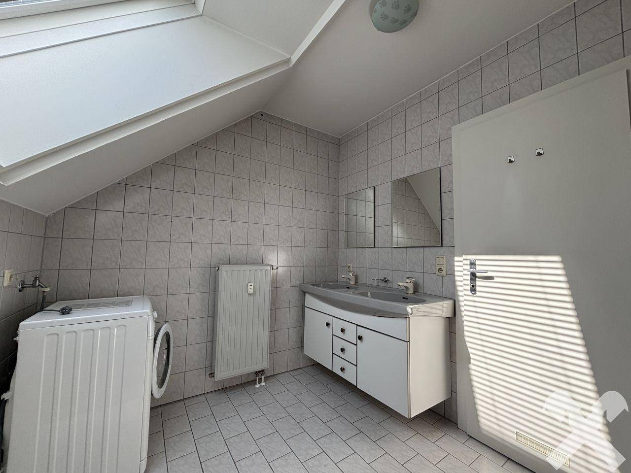 Gefliestes Badezimmer mit Doppelwaschbecken, Dachfenster und Waschmaschine.