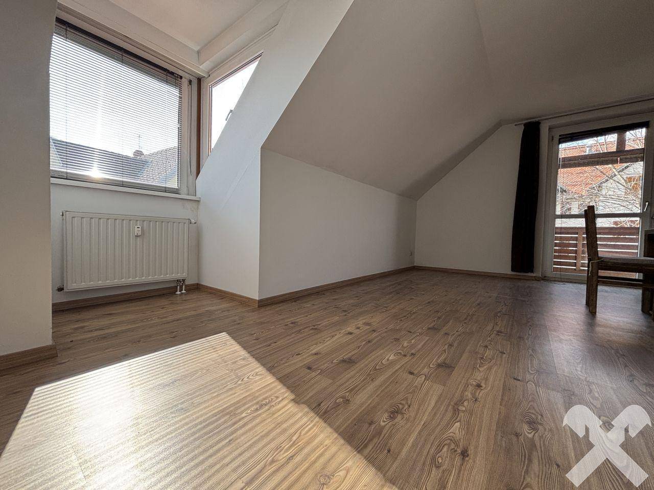 Lichtdurchfluteter Raum mit Laminatboden, Dachschräge und Zugang zu einem Balkon.