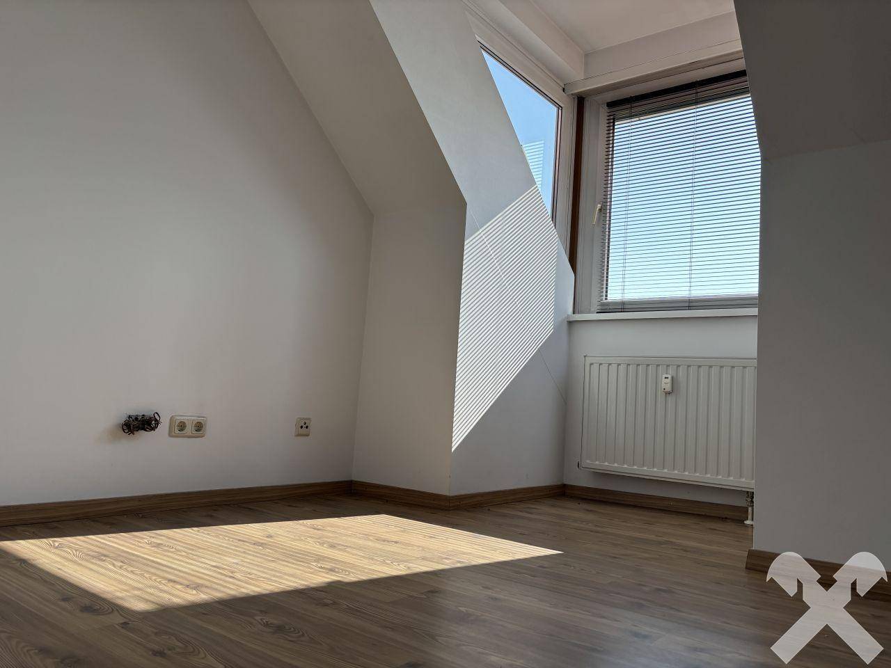 Helles Zimmer mit Laminatboden, Dachschräge und großem Fenster mit Jalousien.