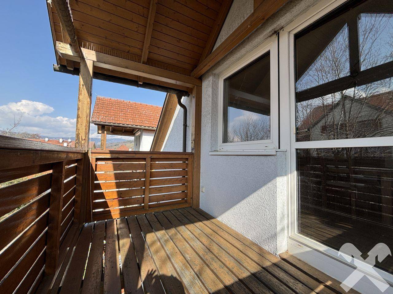 Überdachter Holzbalkon mit Holzboden und Blick auf die umliegenden Häuser.