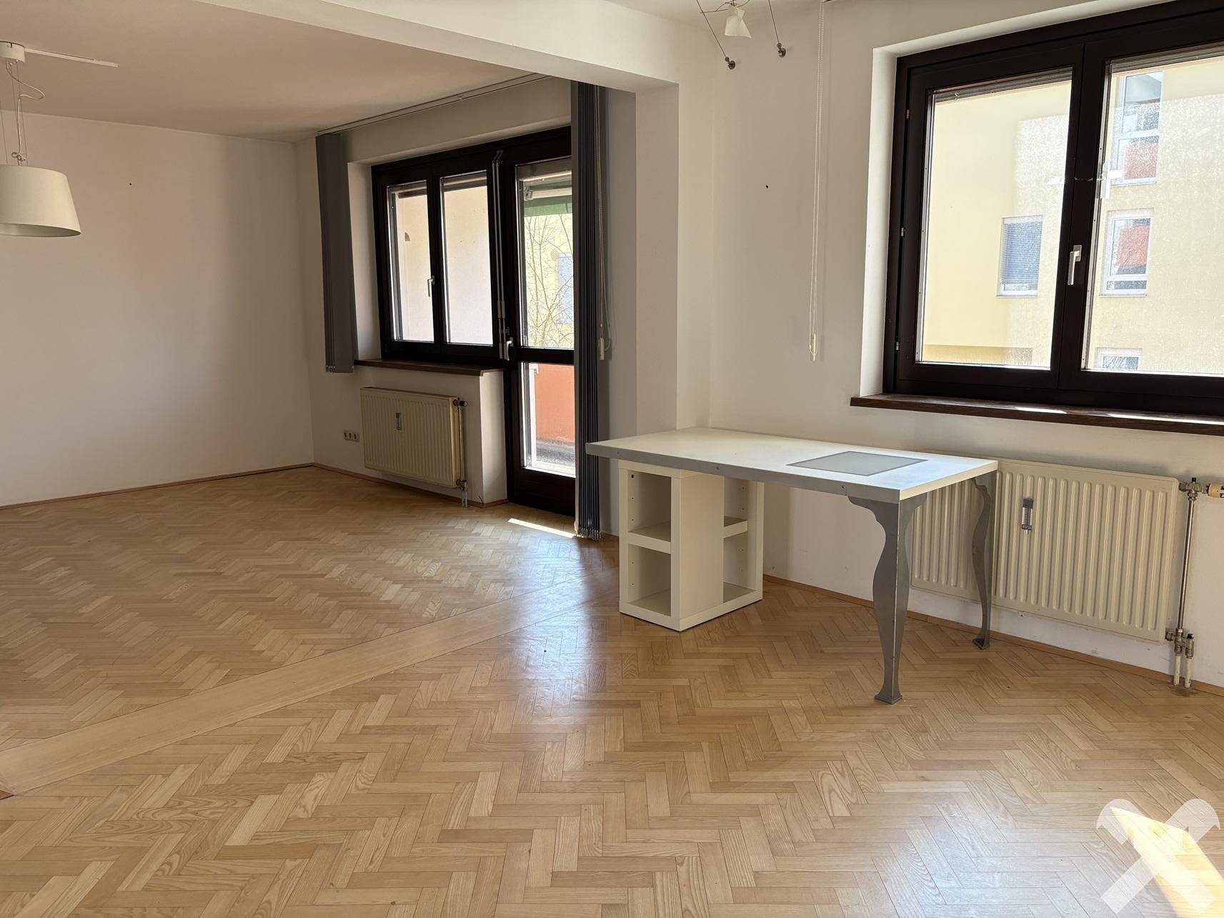 Heller Wohnraum mit Fischgrätparkett und einem Fenster, das den Blick nach draußen freigibt.