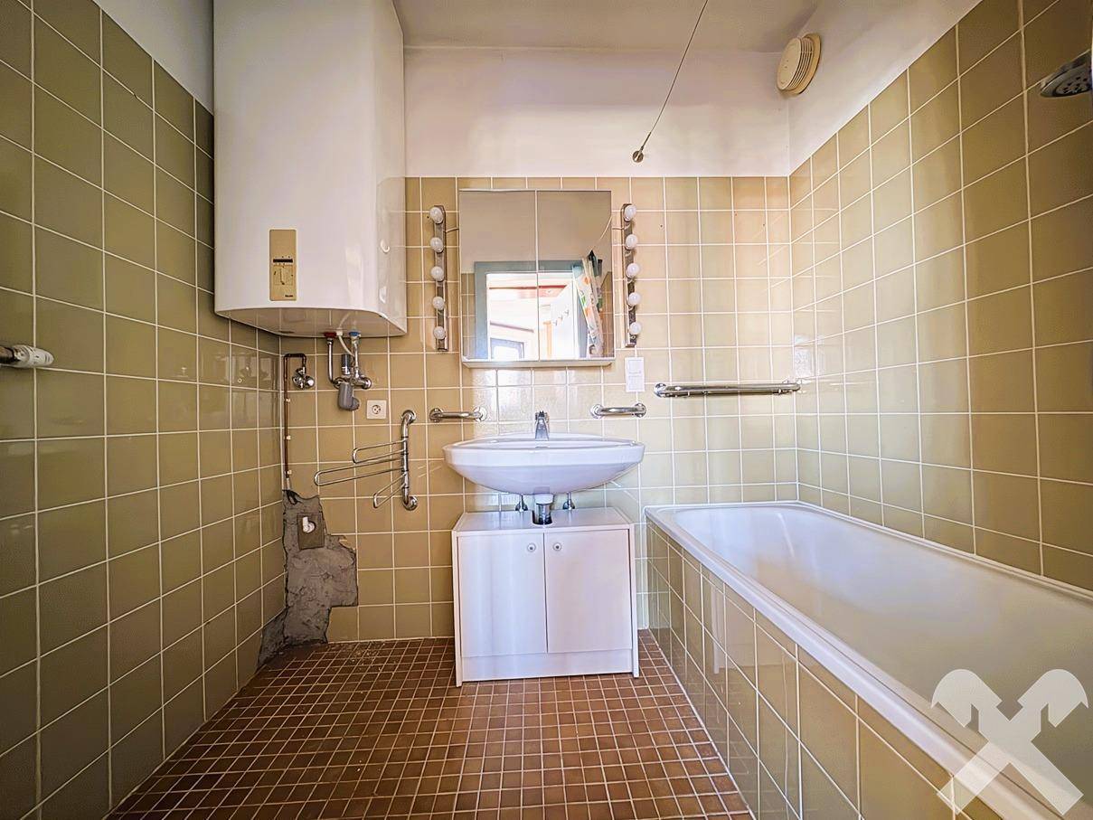 Badezimmer mit Badewanne, Waschbecken und beigefarbenen Fliesen, funktional und hell.