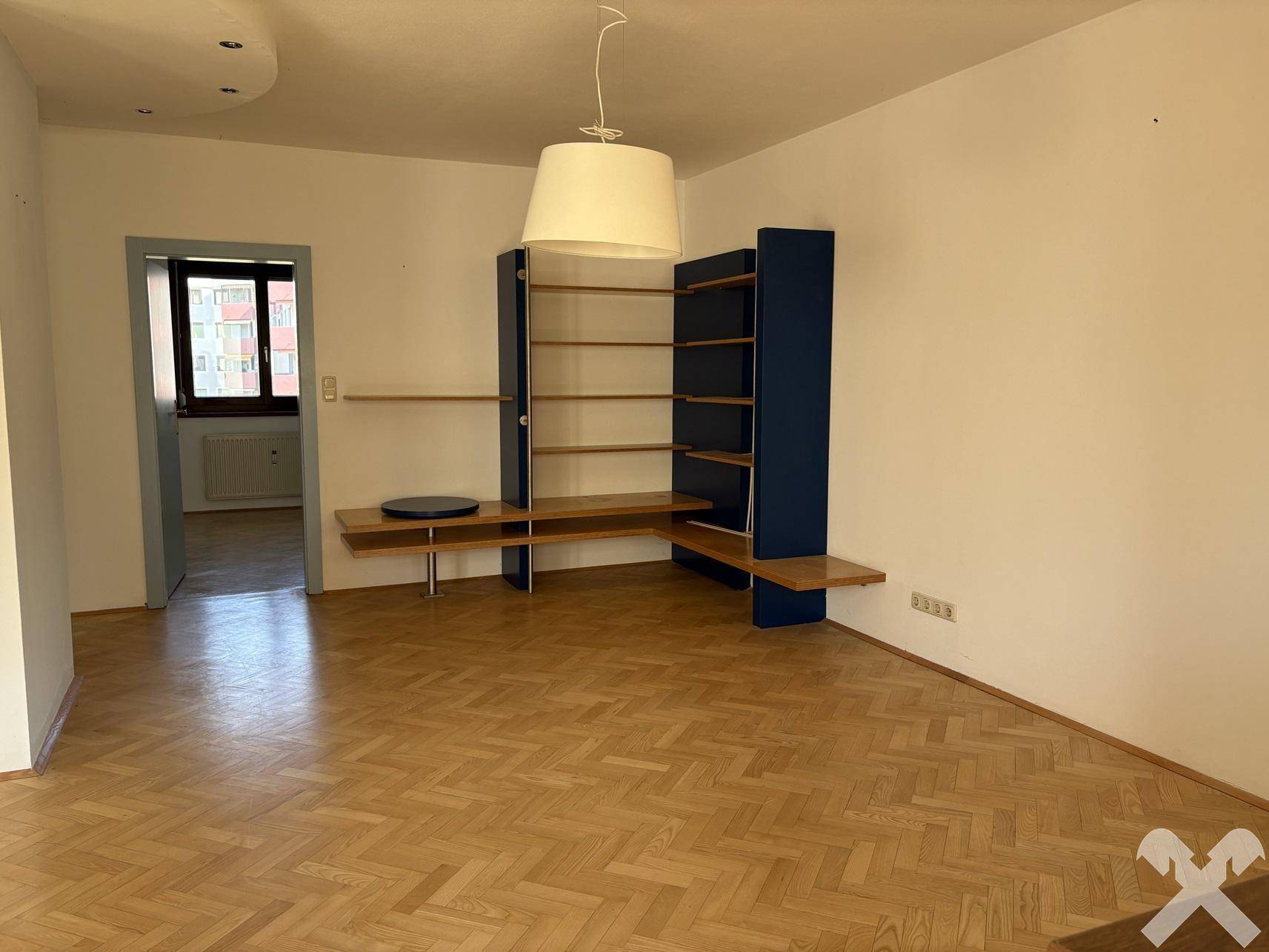 Geräumiger Wohnbereich mit Parkettboden und integriertem Regal, bietet vielseitige Gestaltungsmöglichkeiten.