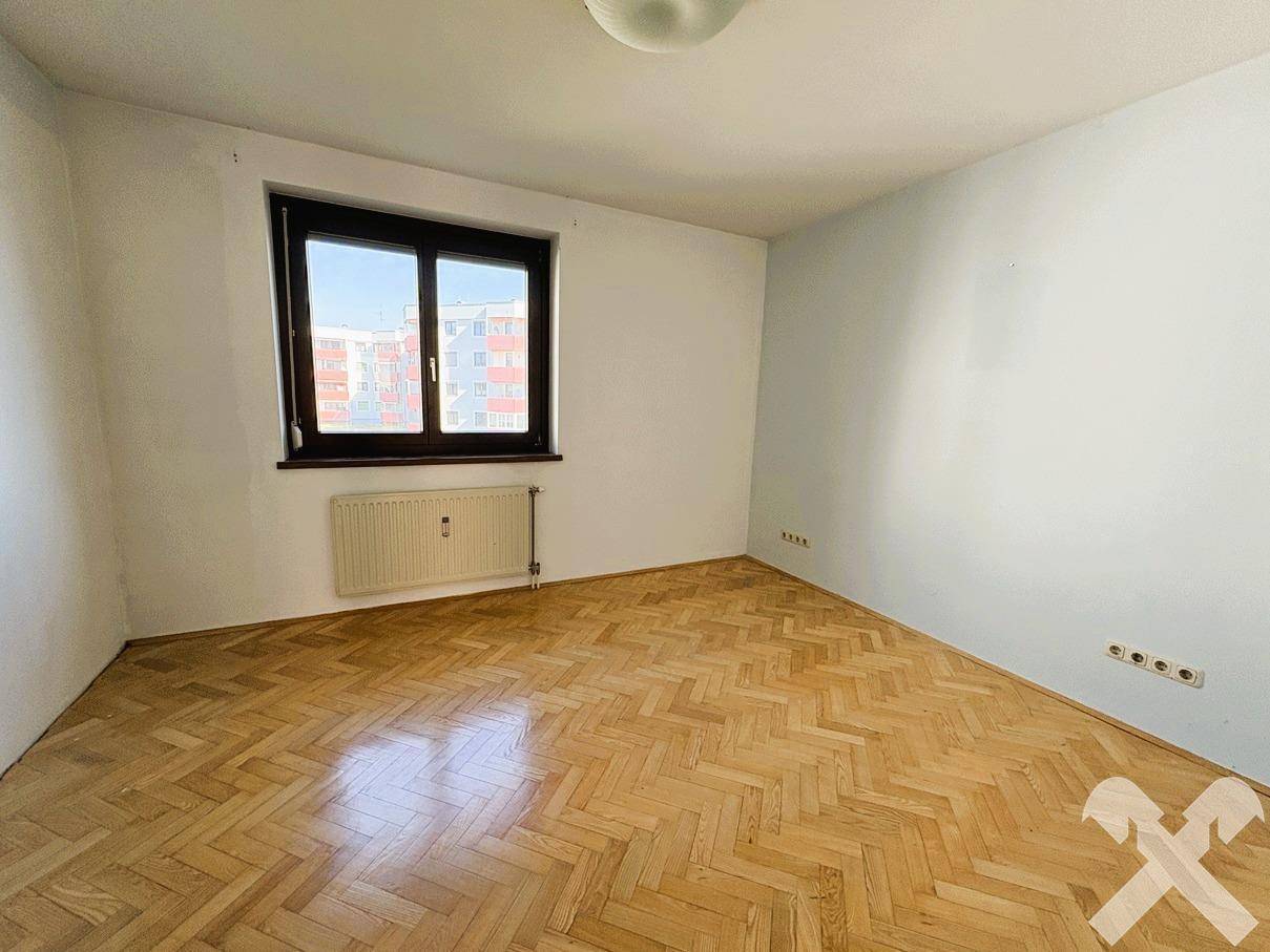 Helles Schlafzimmer mit Parkettboden und Fenster, bietet einen ruhigen Rückzugsort.