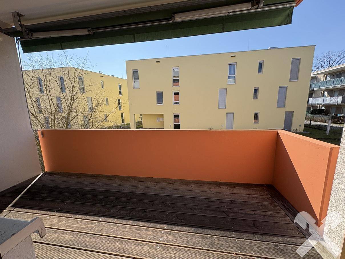 Sonnige Loggia mit Holzboden und Blick auf die umliegenden Gebäude, ideal zum Entspannen.