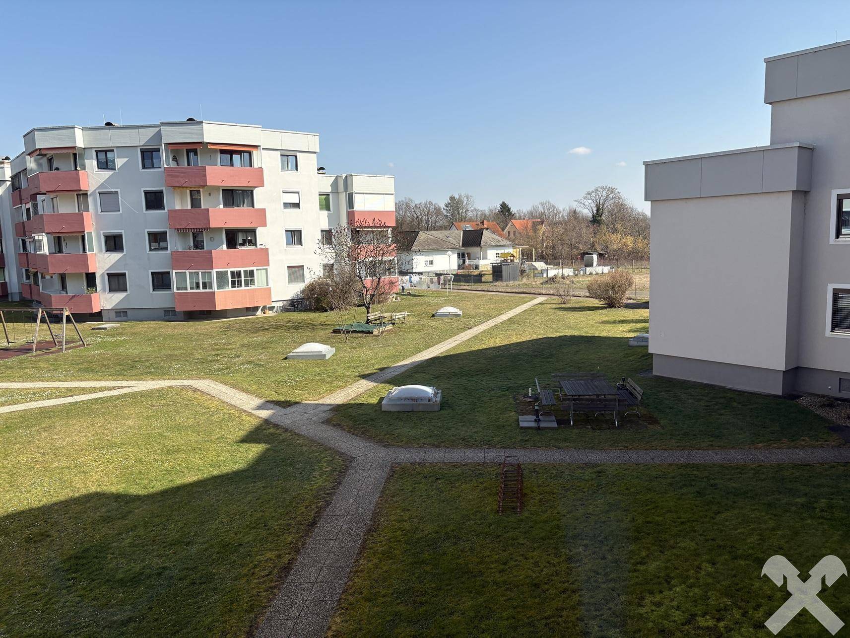 Weitläufige Grünfläche mit Spielplatz und Sitzgelegenheiten zwischen Wohngebäuden, ideal für Familien.