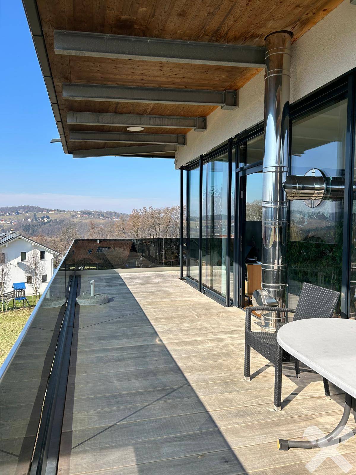 Geräumige Holzterrasse mit Glasgeländer und weitem Blick in die hügelige Landschaft.