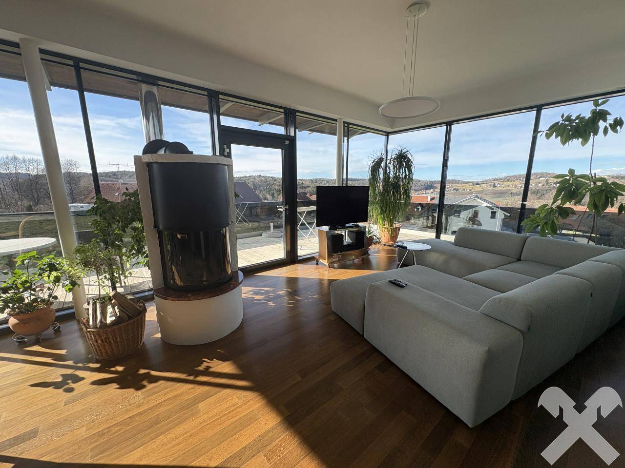 Lichtdurchfluteter Wohnbereich mit Kaminofen, großen Fensterfronten und Panoramablick auf die Landschaft.