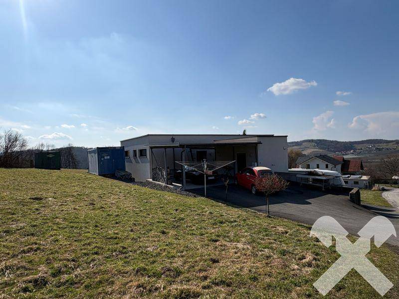 Modernes Gebäude mit Carport und großem Grundstück in ländlicher Umgebung unter blauem Himmel.
